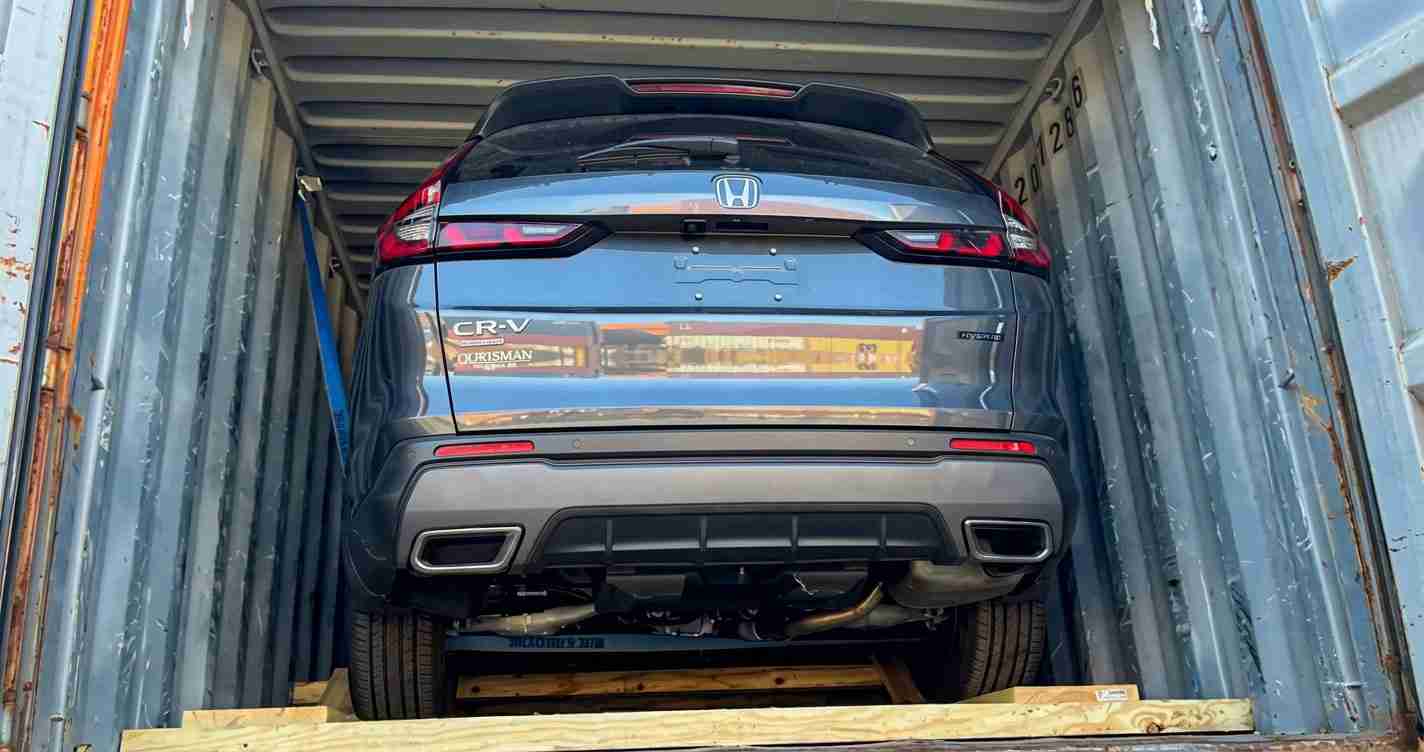 Rear view of a blue Honda CR-V loaded inside a metal shipping container on a wooden pallet, ready for transport.