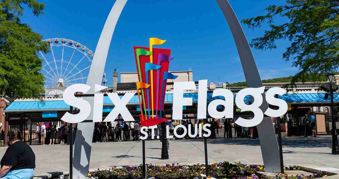 Large 'Six Flags St. Louis' sign with a colorful flag sculpture and a Ferris wheel in the blue sky background.