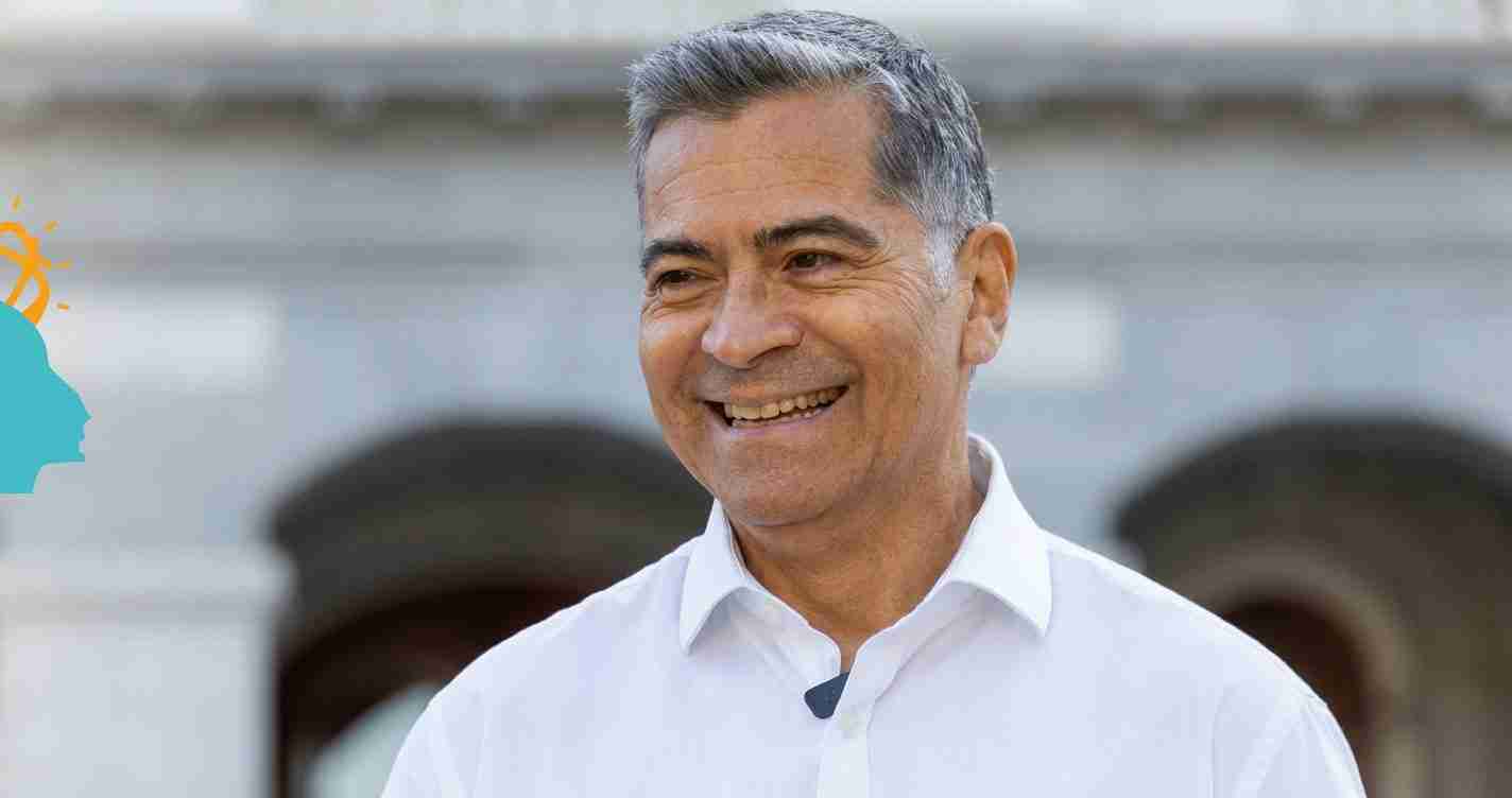 Smiling man in a white shirt outdoors, mic clipped to his chest.
