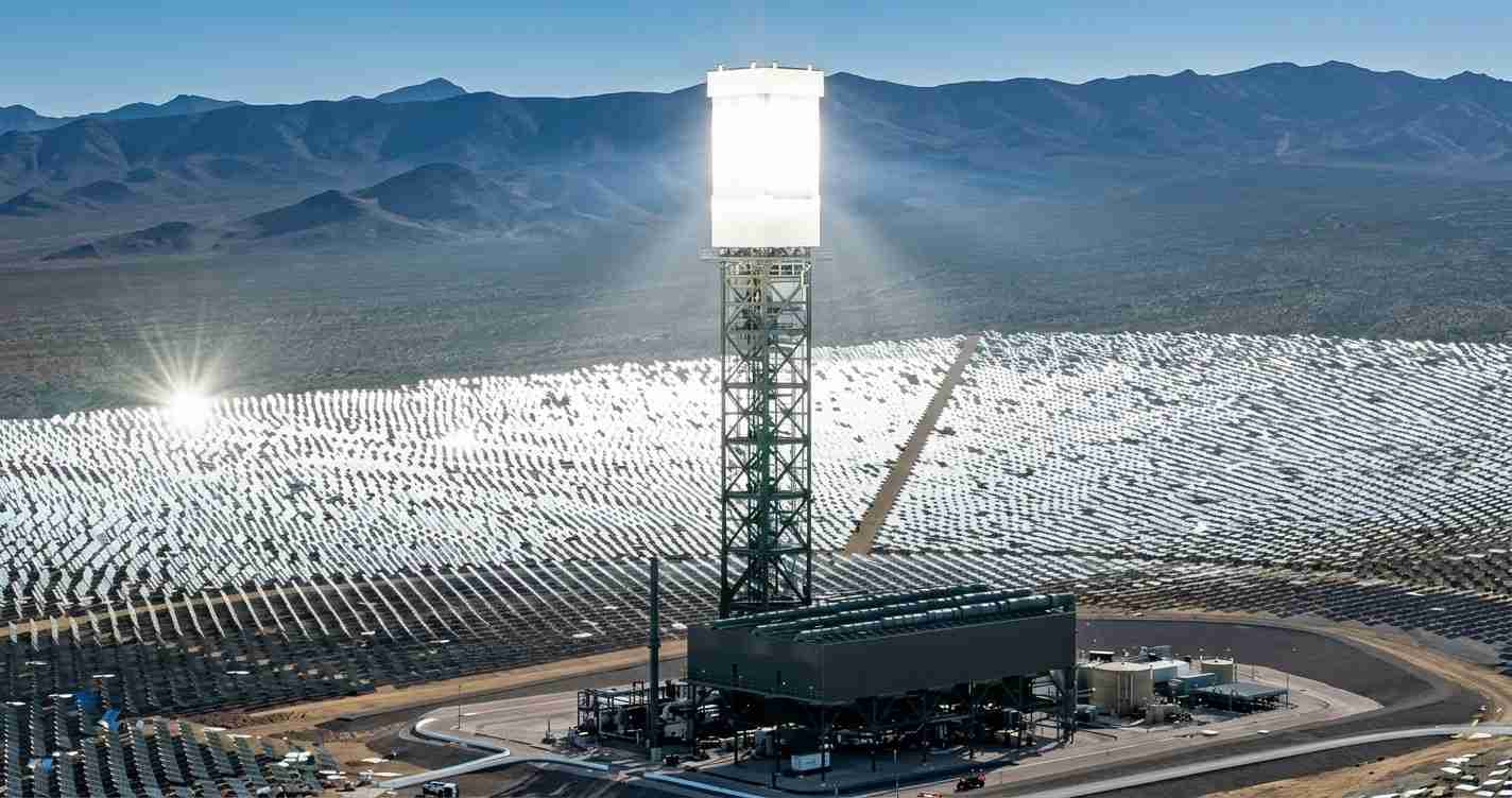 Solar power plant with a central receiver tower and thousands of mirror heliostats in a desert valley.