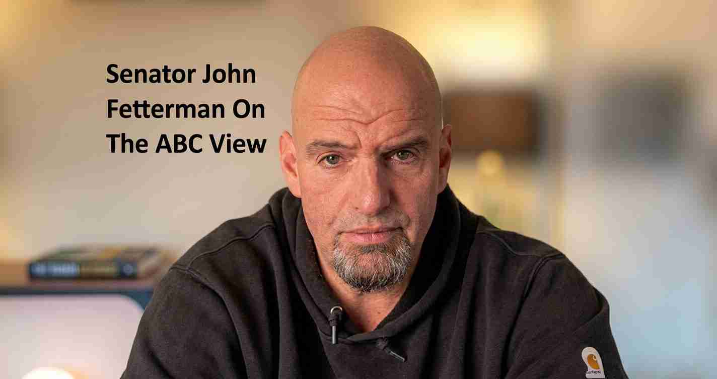 Close-up of a bald man with a goatee wearing a black hoodie, facing the camera; left-side headline text visible.