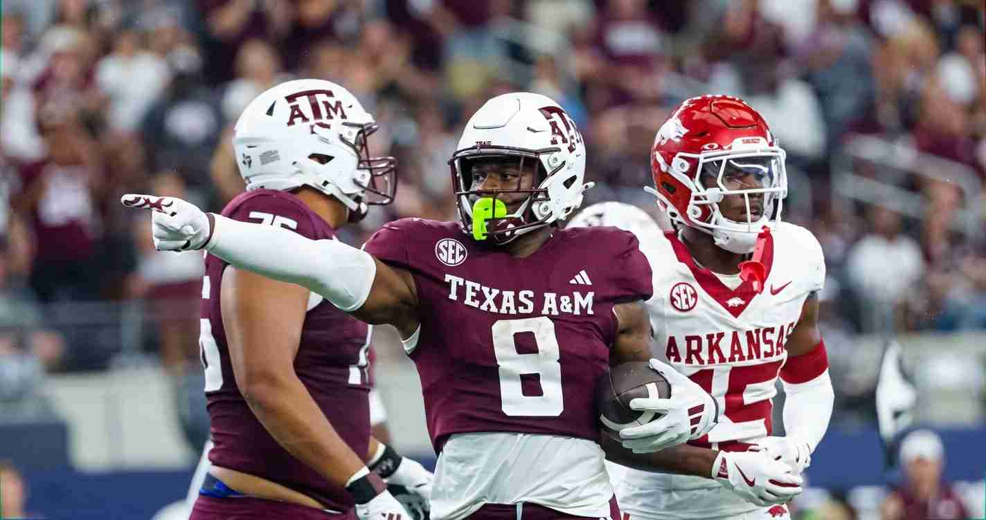 Texas A&M running back in maroon jersey carries the ball as an Arkansas defender closes in.