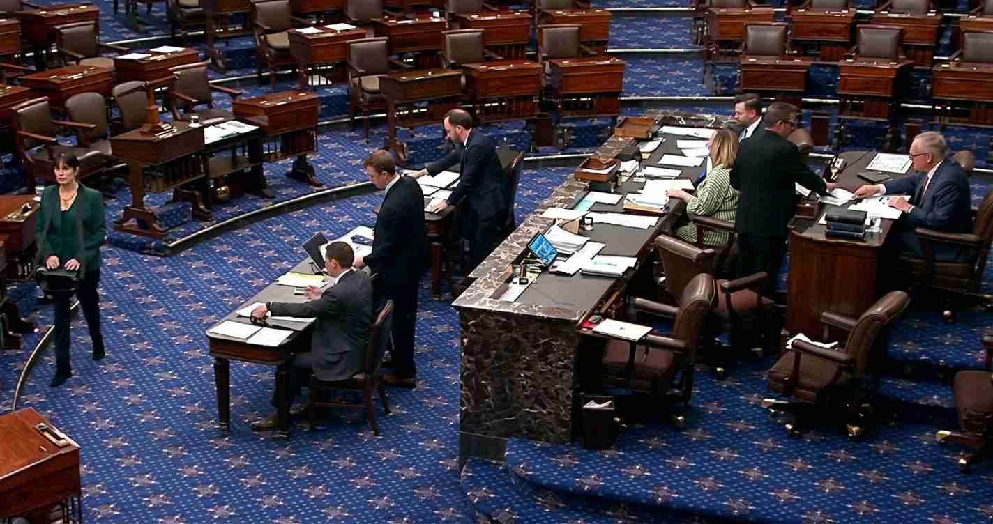 Senate chamber with lawmakers at desks and a marble podium in the foreground during a session.
