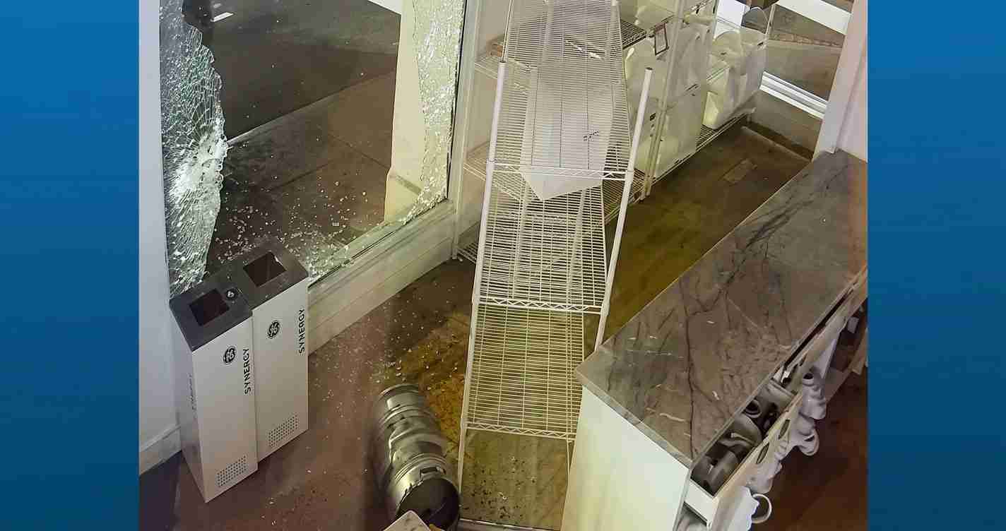 Store interior with a shattered glass window, toppled white wire shelving, and scattered debris on the floor.