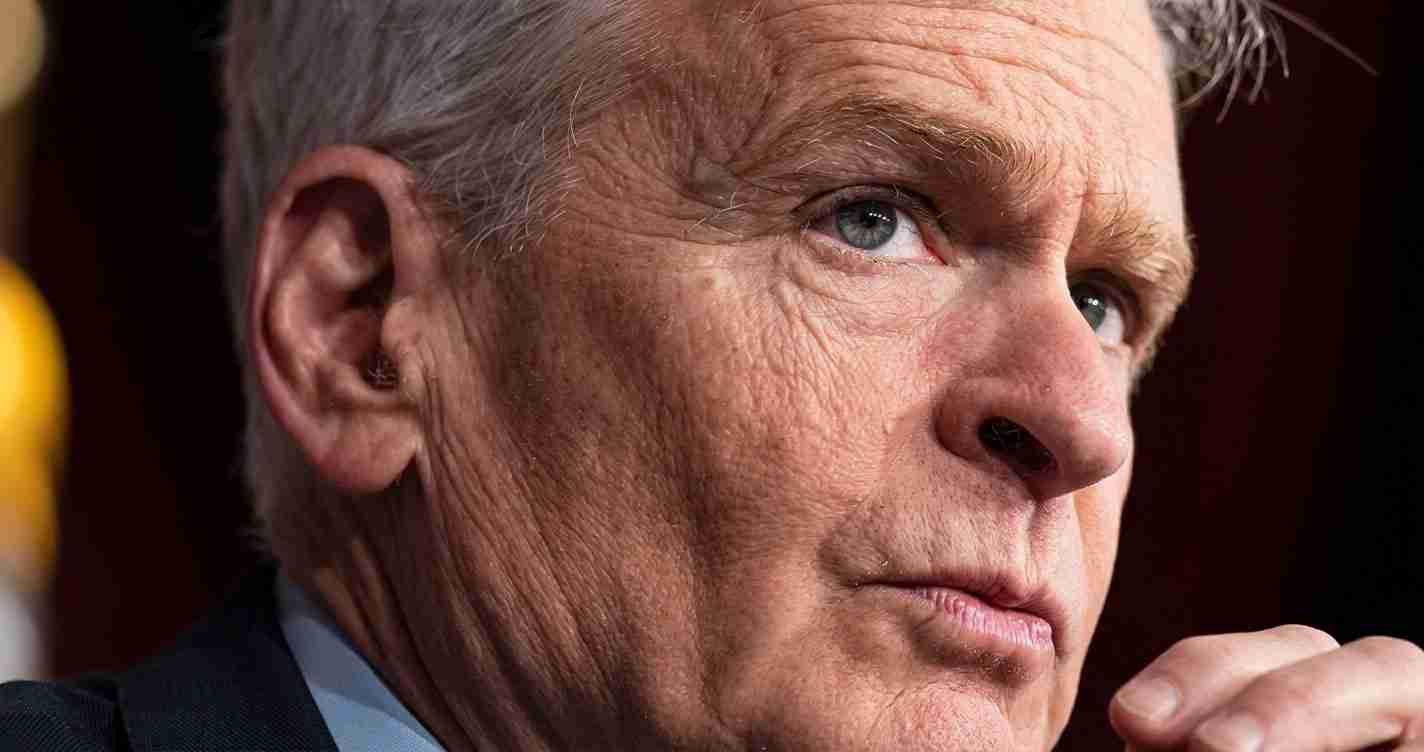 Close-up of a middle-aged man with gray hair and a thoughtful expression, looking to the right.