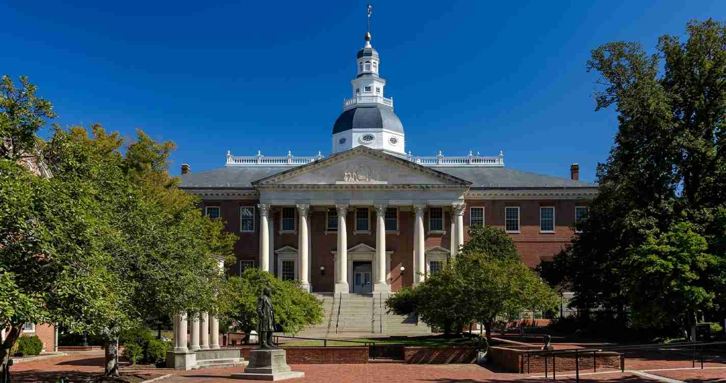 Brick campus building with a white-columned portico and a domed cupola, set against a bright blue sky and green trees on a sunny day.