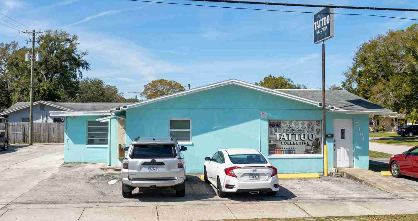 Exterior of a turquoise tattoo shop named 'Tattoo Collective' with two cars parked in front on a sunny day.