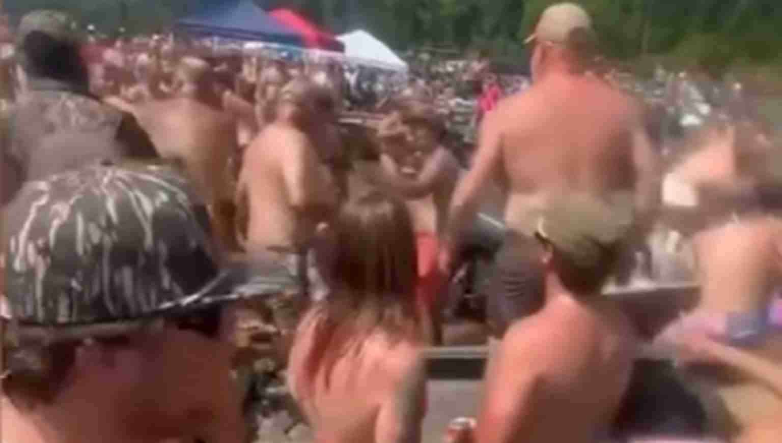 Crowded outdoor beach party with many shirtless people dancing and socializing under sunny skies.