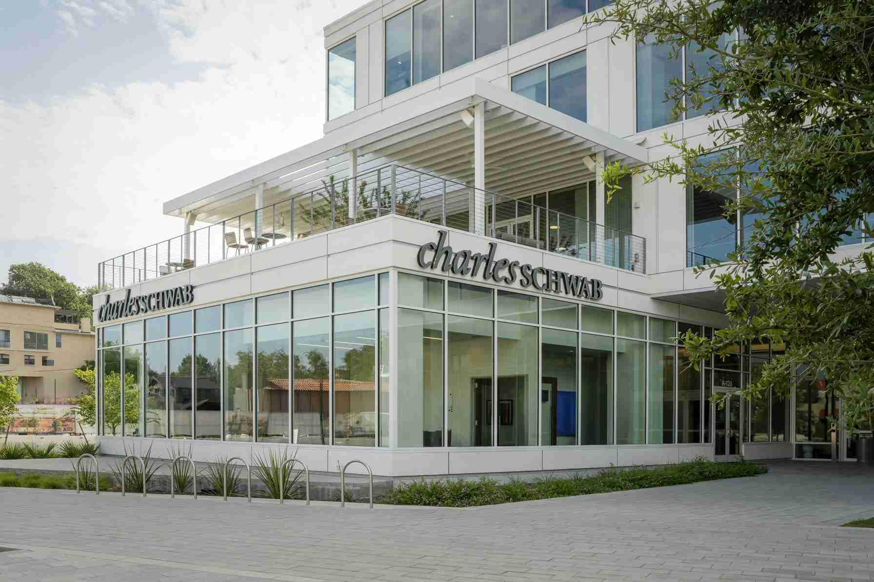 Modern glass-front office building with a prominent Charles Schwab sign along the facade and a second-floor balcony area.