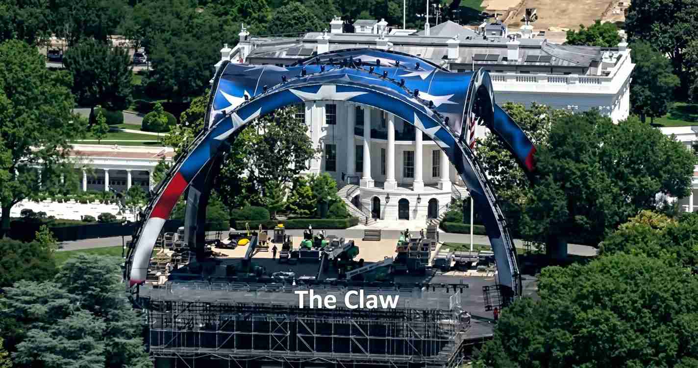 Aerial view of a large outdoor stage with a curved blue–red arch, labeled 'The Claw', set up on a green lawn in front of a white government building.