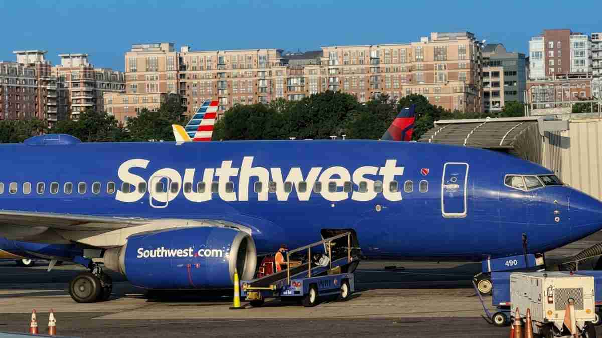 Southwest Airlines jet at a gate with boarding stairs and ground crew near the engine on the tarmac.