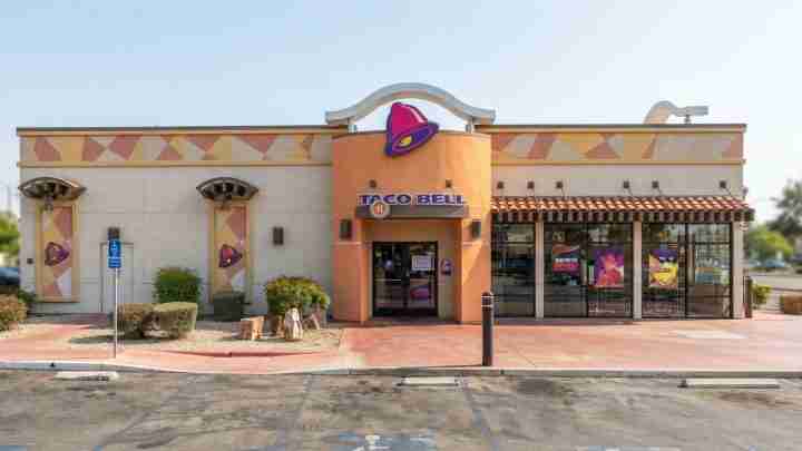 Taco Bell restaurant exterior with a peach-colored entrance and purple bell logo, storefront on the right.