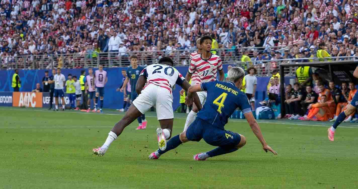 Soccer player in white kit with 20 slides for the ball while a blue-kit defender slides in for a challenge in a crowded stadium crowd.